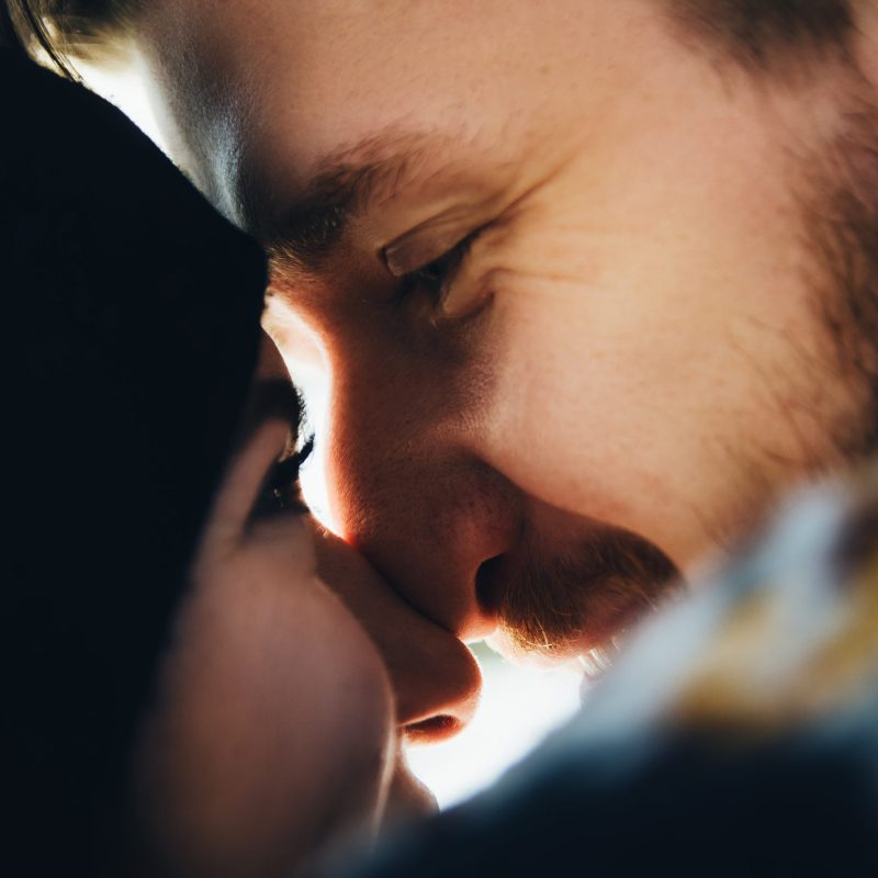 Happy girl in a hat kissing and touches noses boyfriend with a red beard and looking to his eyes. Happy moments. Close up portrait